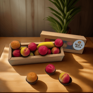 Boîte de fruits déguisés en pâte d'amande avec une étiquette NutsAndCo, contenant des fruits déguisés en pâte d'amande, avec quelques-uns étalés par terre.