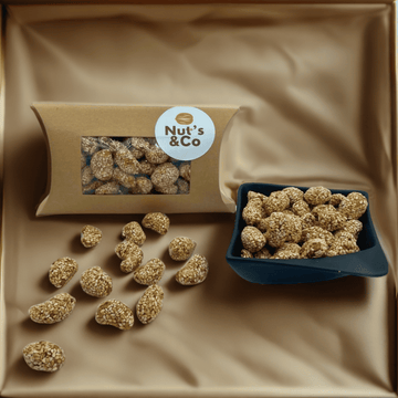 Bol de noix de cajou caramélisées au sésame à côté d’un paquet avec une étiquette NutsAndCo contenant des noix de cajou caramélisées au sésame, avec des noix de cajou étalées par terre.