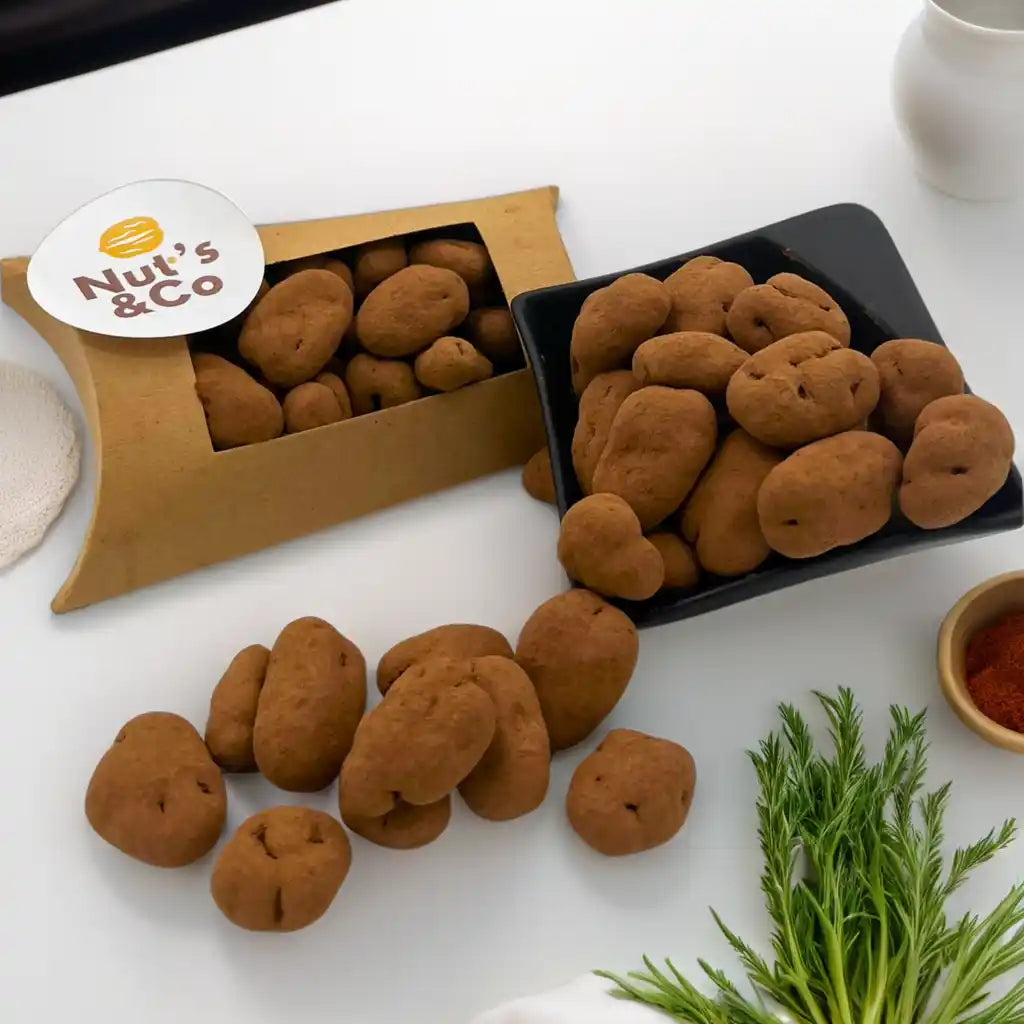 Noix de pécan truffées au chocolat noir posées sur une table, avec un petit bol noir et un paquet NutsAndCo contenant des noix de pécan truffées.