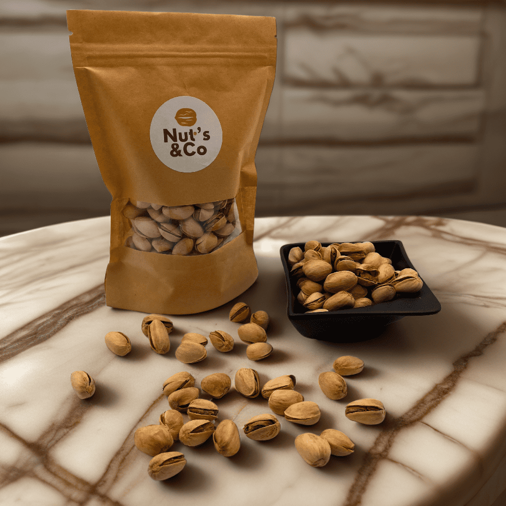 Bol de pistaches finement salées à côté d’un paquet avec une étiquette NutsAndCo contenant des pistaches finement salées, avec des pistaches étalées par terre.